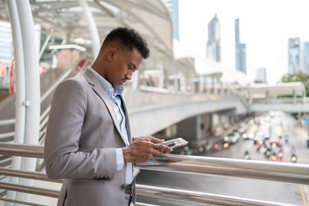 Africa American businessman standing in the city with blur building background holding smartphone...