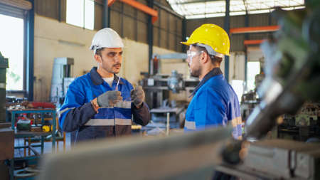 Engineer worker taking in the metal working manufacturing factory and wearing safety helmet and...