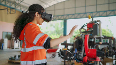 Young Africa American engineer is controlling Futuristic robotic arm with a virtual reality Headset. Testing robot by moving hand at factory. VR Technology industrial and modern equipment.の写真素材
