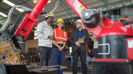 Engineer discuss and brainstorm in the automate robotic arm factory. Welding tool weld metal or plate. Bright sparks and smoke in the production line at Robotic manufacturing. Teamwork and technologyの写真素材