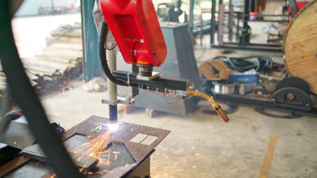 Industrial automate modern robotic welding arm machine tool welds metal and plate. Bright sparks and smoke in the production line at Robotic manufacturing. Technology and AI conceptの写真素材
