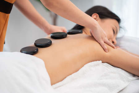 Beautiful woman getting spa hot stone massage in the therapy room at wellness center. Masseuse or...