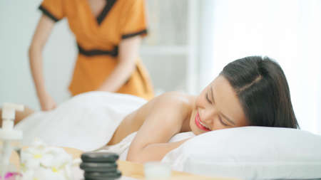 Beautiful woman lying on the spa bed and receiving massage of lower body. Relaxation and revitalization of muscles after work. Therapist massage at arm. Healthy lifestyle and body conceptの写真素材