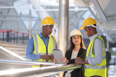 Group of confident engineers and businesswoman wearing helmet and vest standing in the construction...