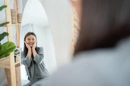Beautiful attractive woman massage on her face and looking at mirror. Feeling happy and relax after apply serum. Enjoy natural clean soft moisturized. Beauty and skin care treatment conceptの写真素材