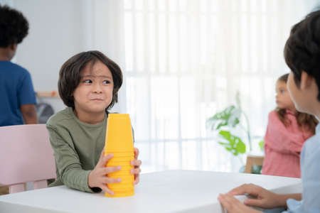 Handsome boys sitting in the kindergarten school classroom and holding cup stacking looking at friend. Learning, enjoy, education, playing concept. Feeling happing and smile during classの写真素材