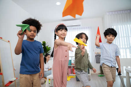 Asia and African kid playing paper rocket in the kindergarten school classroom. Rocket fly in front...
