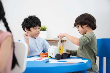 Two handsome boys sitting in the kindergarten school classroom and playing plant toys truck. Boy...
