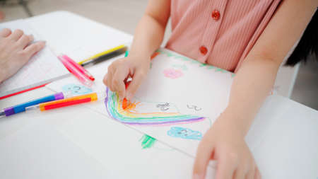 Girls sitting in the kindergarten school classroom with teacher during drawing class. Close up kid...
