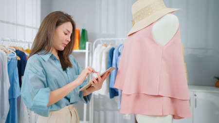 Young Asia woman workin online e-commerce shopping at home. Startup online fashion cloth business. Inspector product and introduce to customer. Buy and sell concept by using wifi technologyの写真素材