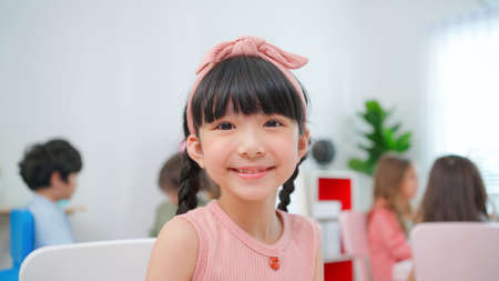 Pretty girls sitting in the kindergarten school classroom with teacher during drawing class. Looking at camera and smile Learning, enjoy, education, playing concept. Feeling happy and funの写真素材