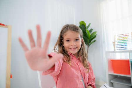 Pretty girls sitting in the kindergarten school classroom and showing hi five to teacher during...