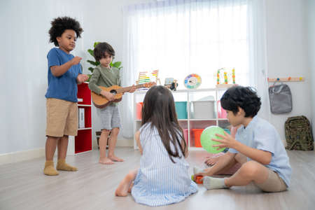 Asia and African boys standing in front of the classroom in the kindergarten school and one kid playing guitar. Group of student sitting on the floor. Learning, enjoy, education, playing concept.の写真素材