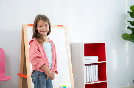 Pretty girls standing in front of the classroom in the kindergarten school looking at camera and smile with copy space. Learning, enjoy, education, playing concept. Feeling happy and fun.の写真素材