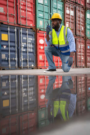 African engineer worker using radio communication and talk with staff. Reflection of the man in the water. Import and export product. Manufacturing transportation and global business conceptの写真素材