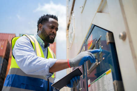 African worker in safety vest press the bottom setting the temperature in the container at shipping yard. Import and export product. Manufacturing transportation and global business conceptの写真素材