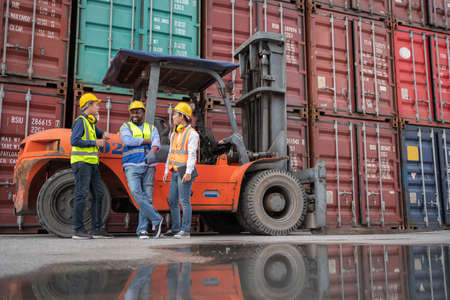 Group of engineer worker standing in front of forklift in the shipping yard container. Talking and rest during break time. Import, export product. Manufacturing transport and global business conceptの写真素材