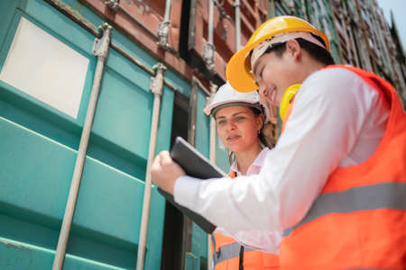 Dock manager woman and engineer worker looking at tablet and check stock in shipping container yard with smile. Import and export product. Manufacturing transportation and global business conceptの写真素材