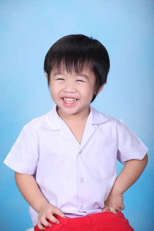 Close up portrait of attractive boy sitting in the studio isolated on blue background with smile. Happy, funny smart boy looking at camera and smile. Lifestyle and pre school conceptの写真素材