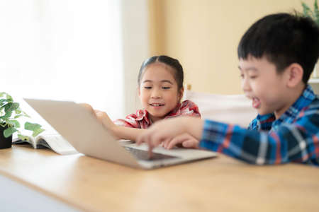 Cute girl and boy sitting in the classroom and doing homework together. Girl looking at laptop and smile play game with her friend. Learning, education and kindergarten concept. Back to schoolの写真素材
