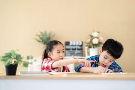 Cute girl and boy sitting in the classroom and doing homework together. Girl ask her friend pick up color pencil. Portrait of school kid. Learning, education and kindergarten concept. Back to schoolの写真素材