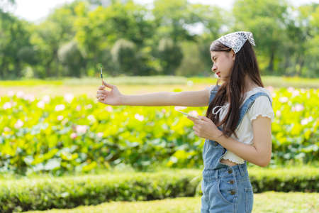 Portrait of attractive young pretty girl standing in the public garden and look at the paintbrush in summer season. Inspiration in green spring park. Art and relaxation on the holidayの写真素材
