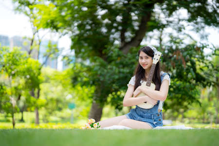 Pretty attractive woman sitting in the garden with blur background. Girl holding Ukulele Guitar on sunny day. Happiness during vacation. Relaxation, Aromatherapy freedom feeling lifestyleの写真素材