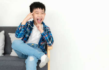 Portrait boy sitting on the soda in the living room isolate on white background. Relaxation and resting after class. Stick out tongue and smile. Feeling happy and fun. Preschool, lifestyle concept.の写真素材