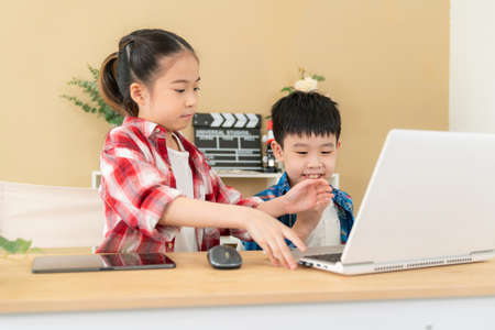 Cute girl and boy sitting in the classroom and doing homework together. Girl looking at laptop and smile play game with her friend. Learning, education and kindergarten concept. Back to schoolの写真素材