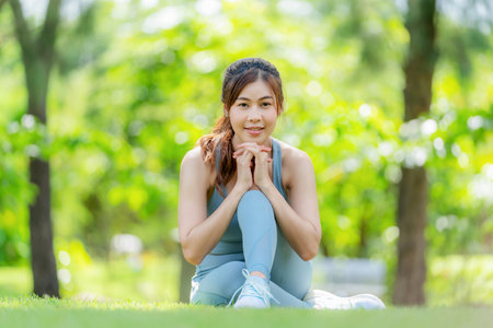 Asia attractive woman in sportswear sitting in the garden and doing yoga with smile. Exercise for flexibility of muscle with copy space under sunlight. Outdoors workout and healthy lifestyleの写真素材