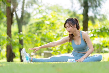 Asia attractive woman in sportswear sitting in the garden and doing yoga with smile. Exercise for flexibility of muscle with copy space before jogging. Outdoors workout and healthy lifestyleの写真素材