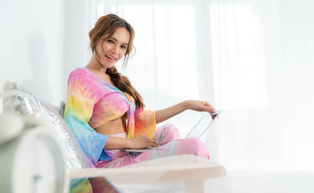 Portrait of attractive pretty woman using laptop while lying on sofa in the living room at home. Happy girl surfing internet with smile. Online working and social network. Relaxation woman concept.の写真素材