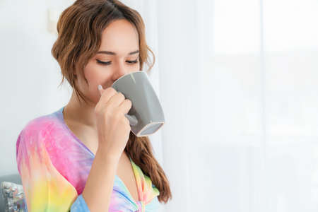 Portrait of attractive pretty woman drinking a cup of coffee while sitting on sofa in the living room at home. Happy girl surfing internet. Online shopping and social network. Relaxation concept.の写真素材