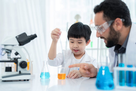 Young Asia kid doing experiment with foreigner teacher in the laboratory at school. Smart boy using...
