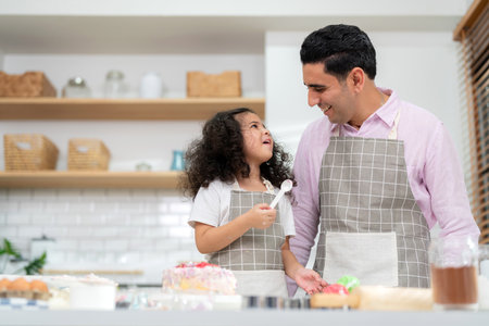 Young little girl standing at counter baking bakery in the modern kitchen at home. Happy smiling and enjoy on weekend. Kids and father wearing apron and smile together. Homemade bakery conceptの写真素材