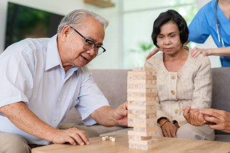 Dementia therapy in playful way. Group of senior elder people stay at nursing home, enjoy activity relation playing tumbling tower wood block game. Training fingers and fine skillsの写真素材