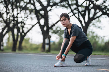 Young modern woman tying running shoes in urban park.の写真素材