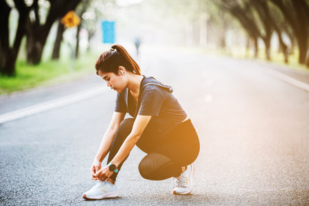 Running shoes - closeup of woman tying shoe laces. Female sport fitness runner getting ready for jogging outdoors on wayの写真素材