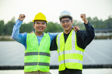 asian engineer and technician standing in solar power plant with arms raisedの写真素材