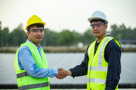 Engineer and technician shaking hands on construction site with solar panel backgroundの写真素材