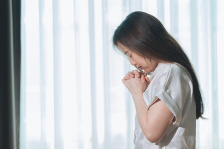Hopeful make wish, calm asian young woman belief, hand in prayer, sitting meditating on sofa at...