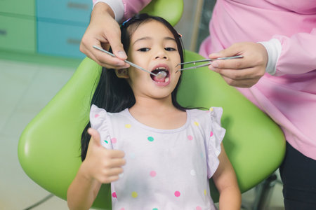 Little asian girl sitting at dental chair with open mouth during oral check up while doctor. Visiting dentist office. Medicine and stomatology concepの写真素材