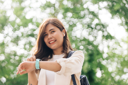 Happy young asian woman walking in the park and using smart watchの写真素材