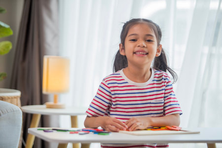 Portrait of smiling little girl sitting at table with book at homeの写真素材