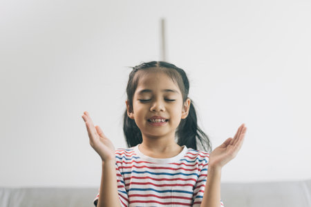 Little asian girl praying on the sofa in the living room.の写真素材