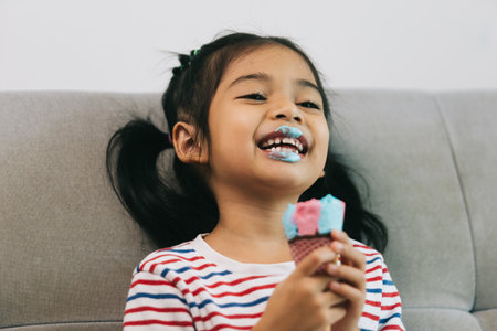 Happy asian little girl eating ice cream on sofa at home.の写真素材