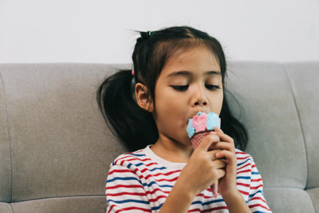 Cute asian child girl eating ice cream on sofa at homeの写真素材