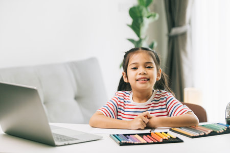 Little asian girl drawing with color pencils and laptop at homeの写真素材