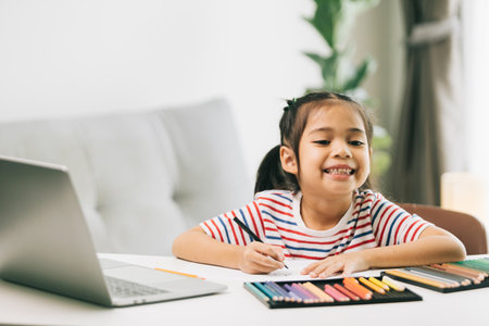 Little asian girl drawing with color pencils and laptop at homeの写真素材