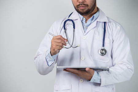 Portrait of male doctor using digital tablet while standing against grey backgroundの写真素材